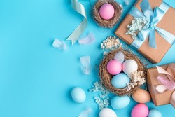 Easter background with colored eggs, nests and gifts on a blue background. Happy Easter. Top view, copy space.