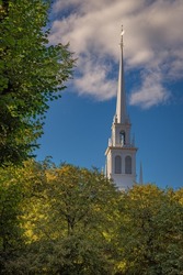 WHITE CHURCH STEEPLE WITH LUSH GREEN FOLIAGE AND BLUE SKIES IN BOSTON