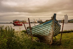 A OLD ABANDONDED FISHING BOAT WITH A SMALL ONE CAR FERRY IN THE BACKGROUND AND A INDUSTRIAL PORT IN CROMARTY SCOTLAND