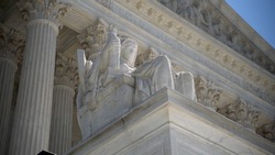 Closeup of sculpture on the Supreme Court building of The Three Fates with Equal Justice slightly out of focus in the distance.