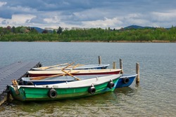 moored rowing boats on a jetty on a lake with scenic view of mountains and clouds in the background