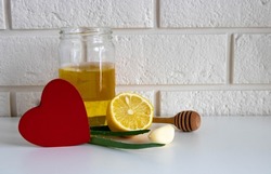 A red wooden heart and natural cold remedies on a white table on a brick background. Garlic, honey, lemon, aloe folk remedies for autumn colds, covid 19.