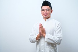 Asian Muslim man wearing glasses smiling to give greeting during Ramadan and Eid Al Fitr celebration over white background