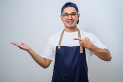 Young handsome asian barista man wearing apron over white background showing product, pointing at something with hands.