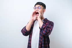 Young asian man wearing casual shirt style shouting and screaming loud to side with hand on mouth over white background. communication concept.