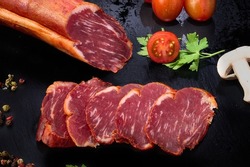 Iberian loin slices on black slate with tomato, parsley, peppercorns and a slice of mushroom