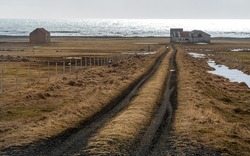 Icelandic meadow land with empty rural road leading to an abandoned farmhouse near the Atlantic Ocean.