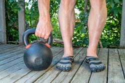 backyard fitness concept - weight training with a heavy iron competition kettlebell on a wooden patio