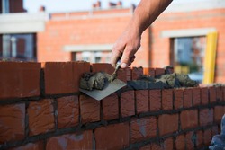 Bricklayer worker installing brick masonry on exterior wall. Professional construction worker laying bricks.