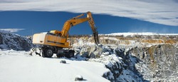 Quarry machine hydraulic breaker works in a winter stone quarry, against a blue sky with clouds, panorama.