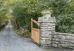Gate post with wooden gate open to a long driveway lined either sdie by trees