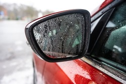 Fine water droplets on a side mirror of a red car.