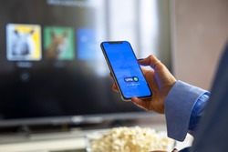 Person holding a smartphone connected to a VPN while watching shows on a streaming service on Television.