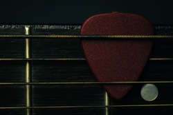 red guitar pick tucked into gold acoustic guitar strings on a dark wood fret board.