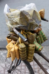 Vietnamese street food being delivered or sold from an old bicycle. A plastic bag protects from the light rain. Banana Leaves are stuffed with rice.