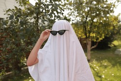 Concept of Halloween, Ghost with sunglasses. a girl in the role of a ghost runs on green grass. funny ghost in glasses
