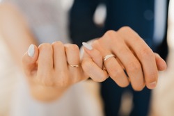 Newlyweds hold hands, hold hands together with little fingers, holding hands together in the foreground, close-up of the hands of a young couple with wedding rings on their ring fingers
