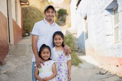 Latino father with his two happy daughters outside his house in rural area-Hispanic father hugging his daughters