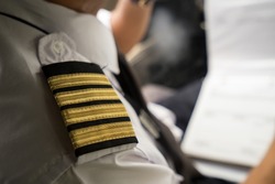 Captain in the aircraft cockpit writing a report after flight. Focusing on his pilot epaulets.