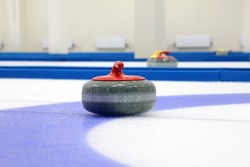 A curling stone with a red handle was shot close-up on ice
