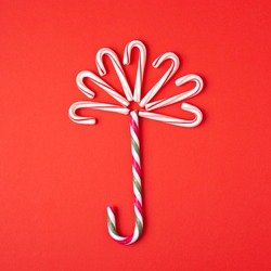 Umbrella made of candy cane lollipop on red background. Minimal styled card.