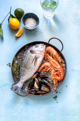 Fresh seafood: shrimp, mussels and dorado fish, on ice in a copper cup, with lemon, lime, sea salt. On a blue background. top view overhead view   copy space