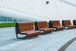 Recreation area with empty contemporary wooden benches along white curved wall near modern business centre.Urban public vandal proof furniture.Public city resting area design.