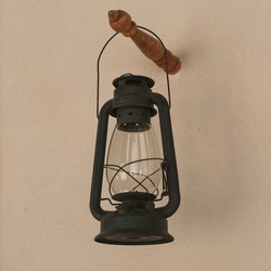 Vintage black gasoline lantern hanging on stucco wall background after renovation . Antique obsolete repaired kerosene lamp close up. Old oil lamp