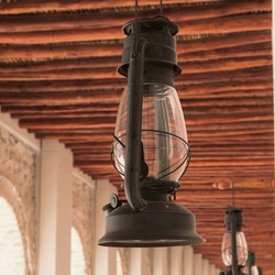 Selective focus to vintage repaired black gasoline lantern is hanging on blurred corridor background  . Antique obsolete kerosene lamp close up. Old oil lamp.