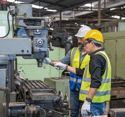 Male Factory engineer and male worker in safety work uniform (hard helmet and vest) are checking heavy machinery in an industrial manufacturing factory, Factory workers concentrate with heavy machine