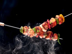 BBQ chicken skewers grilled with vegetables, on a black background