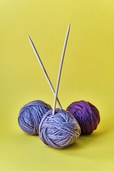 Composition of three purple balls of acrylic yarn and two wooden spokes on yellow background. Craft concept.