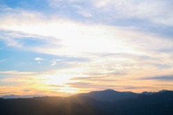 Mountain panorama from a bird's eye view. The sky above the mountain peaks at sunset. Bright multi-colored clouds, the sun's rays pass through the air and make orange, yellow, pink reflexes