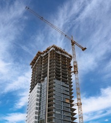 A construction crane builds a tall downtown apartment building in Calgary Alberta Canada.