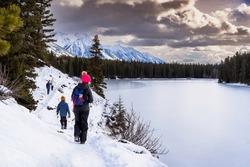 A group of people walking on a winter hiking trail along Johnson Lake in Banff National Park Canada