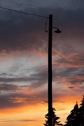 A street lamp on an old wooden telephone pole silhouette under a sunset sky background in Alberta Canada.