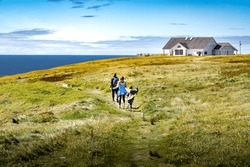 Family on vacation running across a grassy field overlooking high cliffs and the Atlantic Ocean at Cape St. Mary's Ecological Reserve Newfoundland Canada.