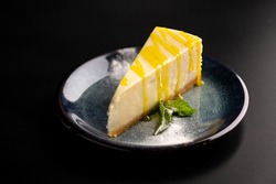 Sweet dessert on a plate on a black background. Classic cheesecake with yellow lemon syrup. Copy space.