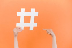 Horizontal images of female hands holding and pointing on large big hashtag sign, viral web content, internet promotion, isolated on pastel orange studio wall. Blogging blog website strategy concept