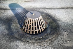 Caged roof drain on flat roof with 2-ply SBS or modified bitumen roofing system. Inspect, maintain and repair roof drainage system to prevent water damage. Selective focus.