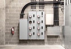 Electrical room with multiple smart meters, cabinets, wiring and fire extinguisher. Below-grade service room of 4 story strata building with residential or commercial units. Selective focus.