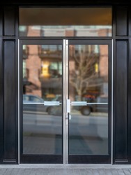Exterior building entrance with black steel double glass door and defocused reflection from traffic and neighboring building. Commercial, business or residential lobby entrance. Selective focus.