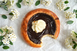 Traditional czech baked pastry product - yeast dough kolache with dark plum preserve (povidla) and quark cheese (tvaroh). Kolach is lying on a paper surface with white flowers