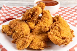 deep fried southern style breaded chicken tenders or chicken fingers on a white plate with dipping sauce