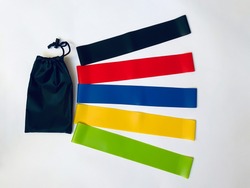 a set of colorful latex rubber bands for fitness and a black cover for them on a white background.  sports concept.  top view, flat lay, copy space