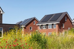 Solar panels on the roof of new built houses in The Netherlands collecting green energy from the sun in a modern and sustainable way. New technology on Dutch houses surrounded by nature, poppy flowers