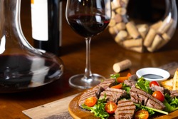 close up of grilled beef tenderloin fillet with rocket salad and cherry tomatoes pairing with Italian fine red wine bottle, glass and decanter in a wooden table classic vintage elegant moody style