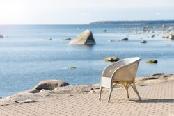 Beach cafe chair with blurred sea background. Summer vacation, travel, holidays concept. Lonely, empty, white wicker seat on shore pavement in sunshine. Seaside restaurant on sunny day. Soft focus