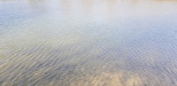 Gray and brown lake water surface with slight ripples from light wind and small shadows on the water (angle, texture).