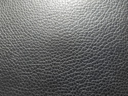 Black imitation leather with small mesh print on the chair (macro, top view, texture).
